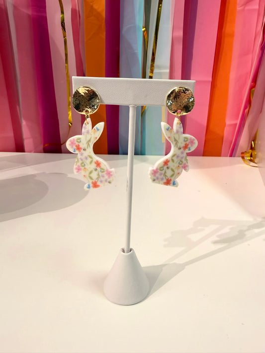 Doodles by Rebekah floral bunny statement earrings featuring hand-drawn spring wildflower patterns and hammered gold studs. These colorful Easter-themed accessories are shown against a bright party streamer backdrop.