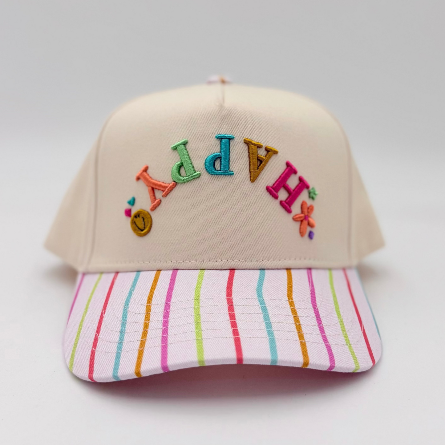 Beige cap with colorful letters and a striped pink and blue visor on a light gray background