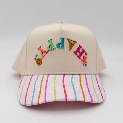 Beige cap with colorful letters and a striped pink and blue visor on a light gray background
