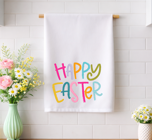 Whimsical "Happy Easter" decorative tea towel with colorful hand-drawn typography, hanging in a bright spring kitchen with fresh floral accents.