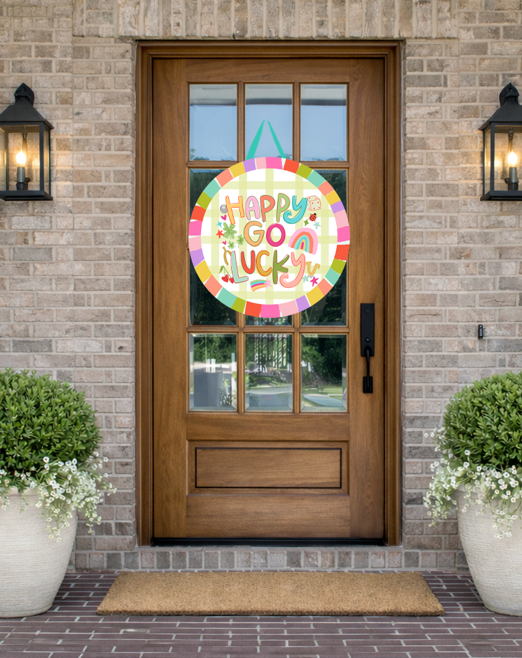 Doodles by Rebekah St. Patrick's Day door decor featuring a whimsical "Happy Go Lucky" illustration with rainbow and shamrock motifs on a rustic front porch.