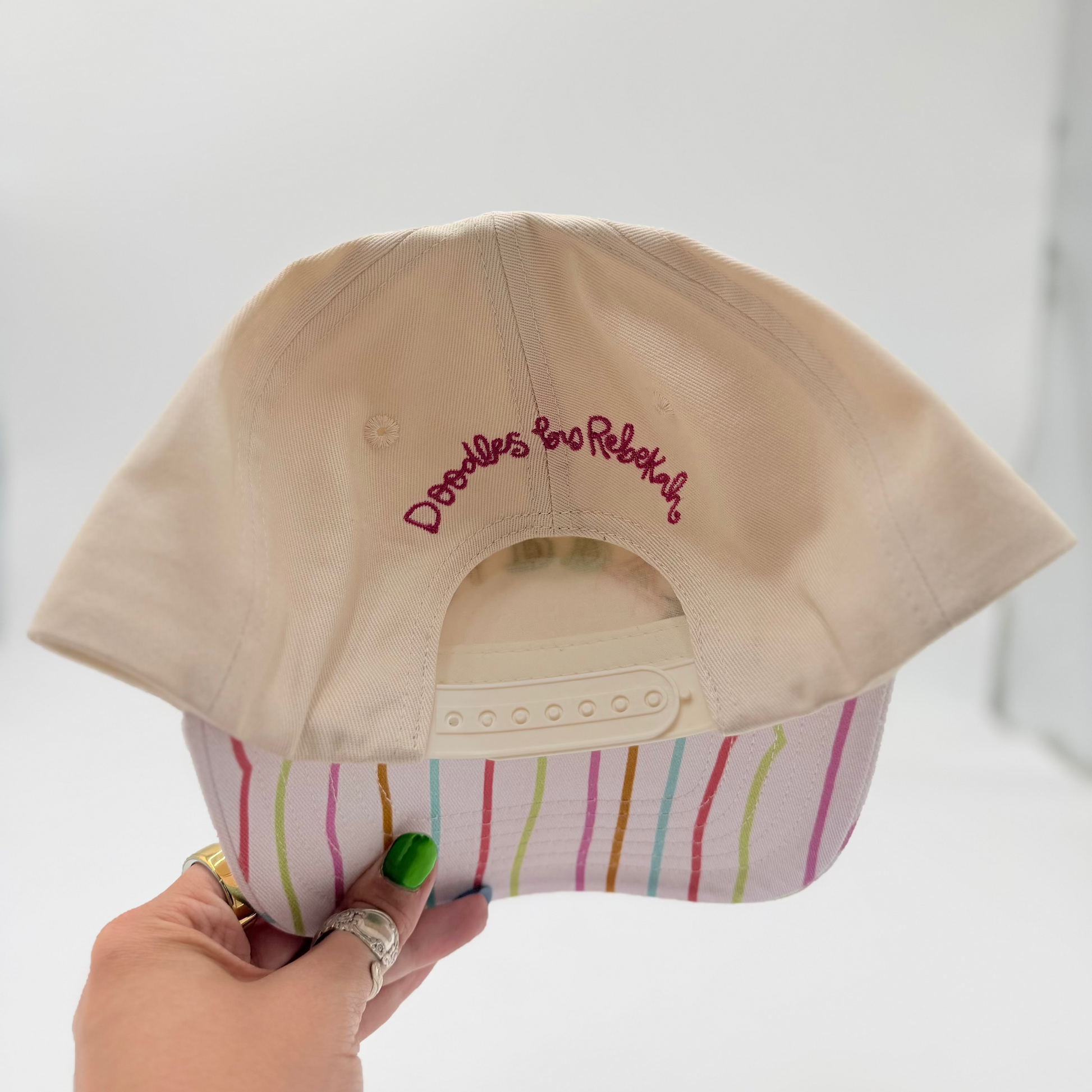 Beige cap with embroidered text held by a hand against a white background