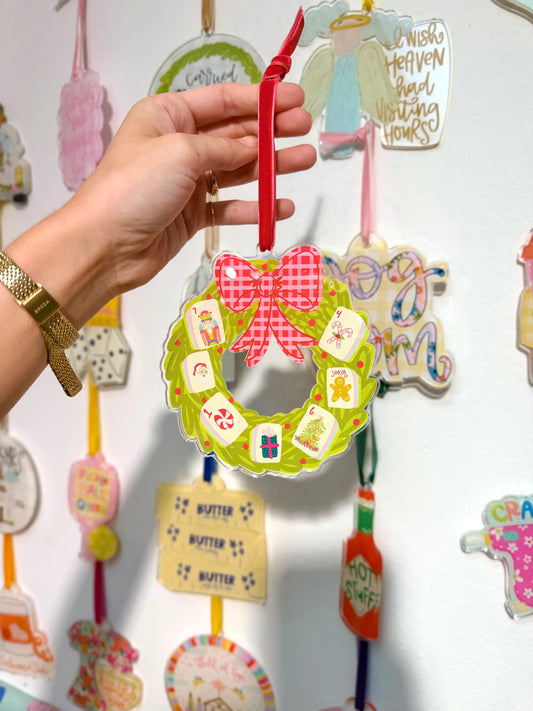 A Mahjong wreath acrylic ornament being held in front of an ornament wall