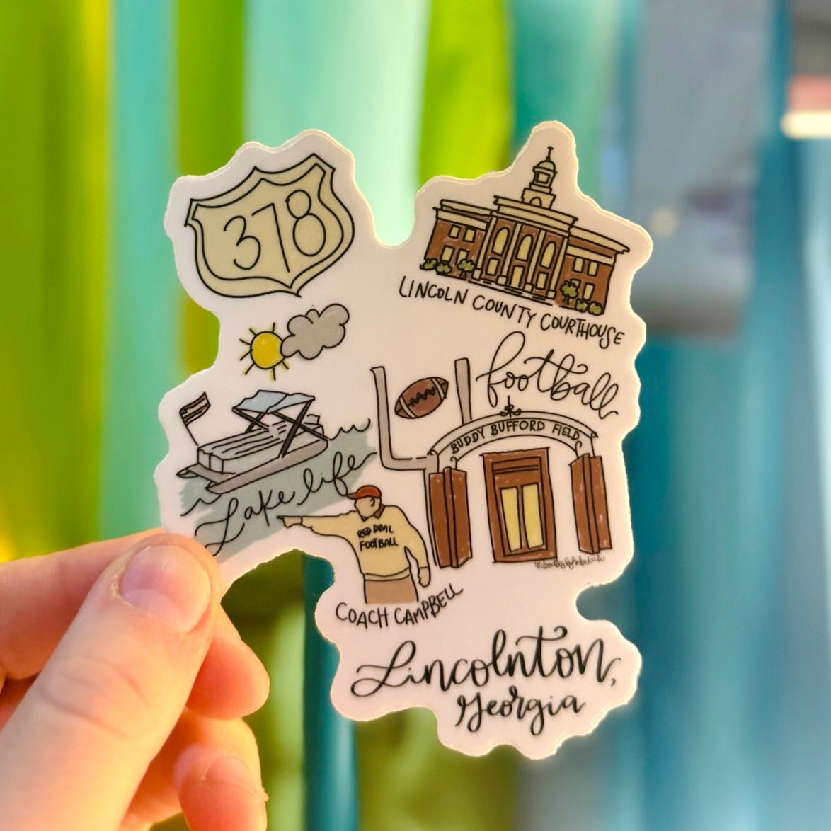 Doodles by Rebekah Lincolnton, Georgia landmarks vinyl sticker. This whimsical hand-painted decal features local favorites like Buddy Bufford Field and the Lincoln County Courthouse, making it a perfect hometown gift or souvenir for water bottles, laptops, and planners.