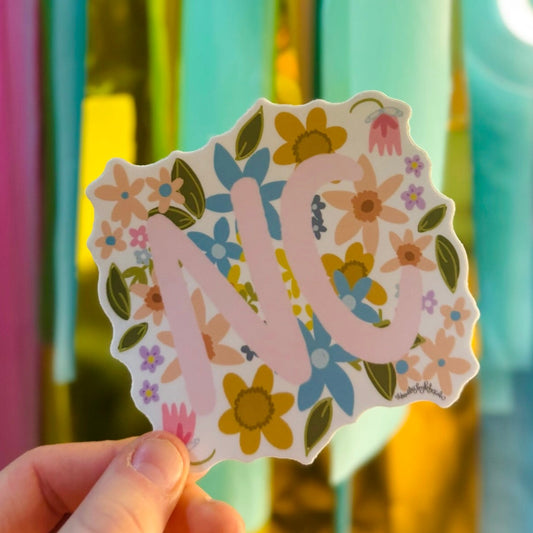 Doodles by Rebekah North Carolina "NC" state pride floral sticker. This whimsical hand-painted vinyl decal with botanical accents and pink lettering is a perfect gift for North Carolinians to decorate water bottles, laptops, and planners.