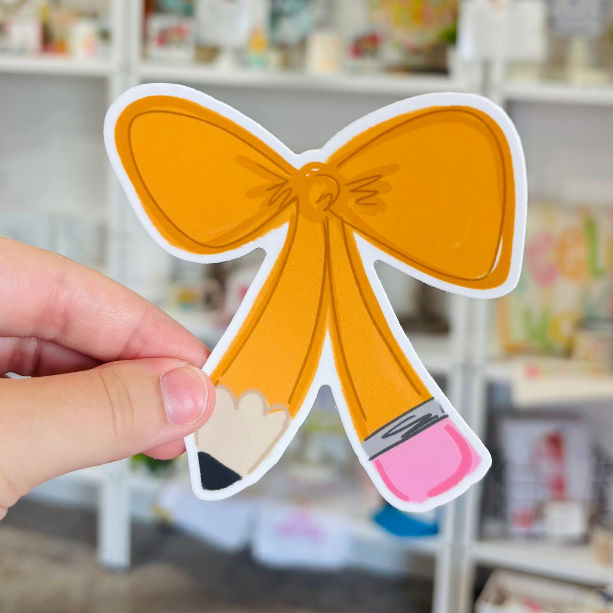 a hand holding a sticker of a pencil tied into a bow