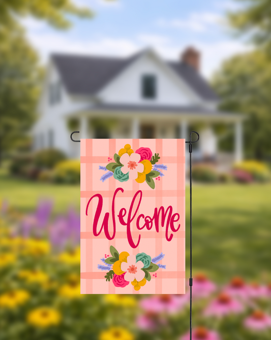 Decorative garden flag with 'Welcome' text and floral designs in front of a house with a garden.