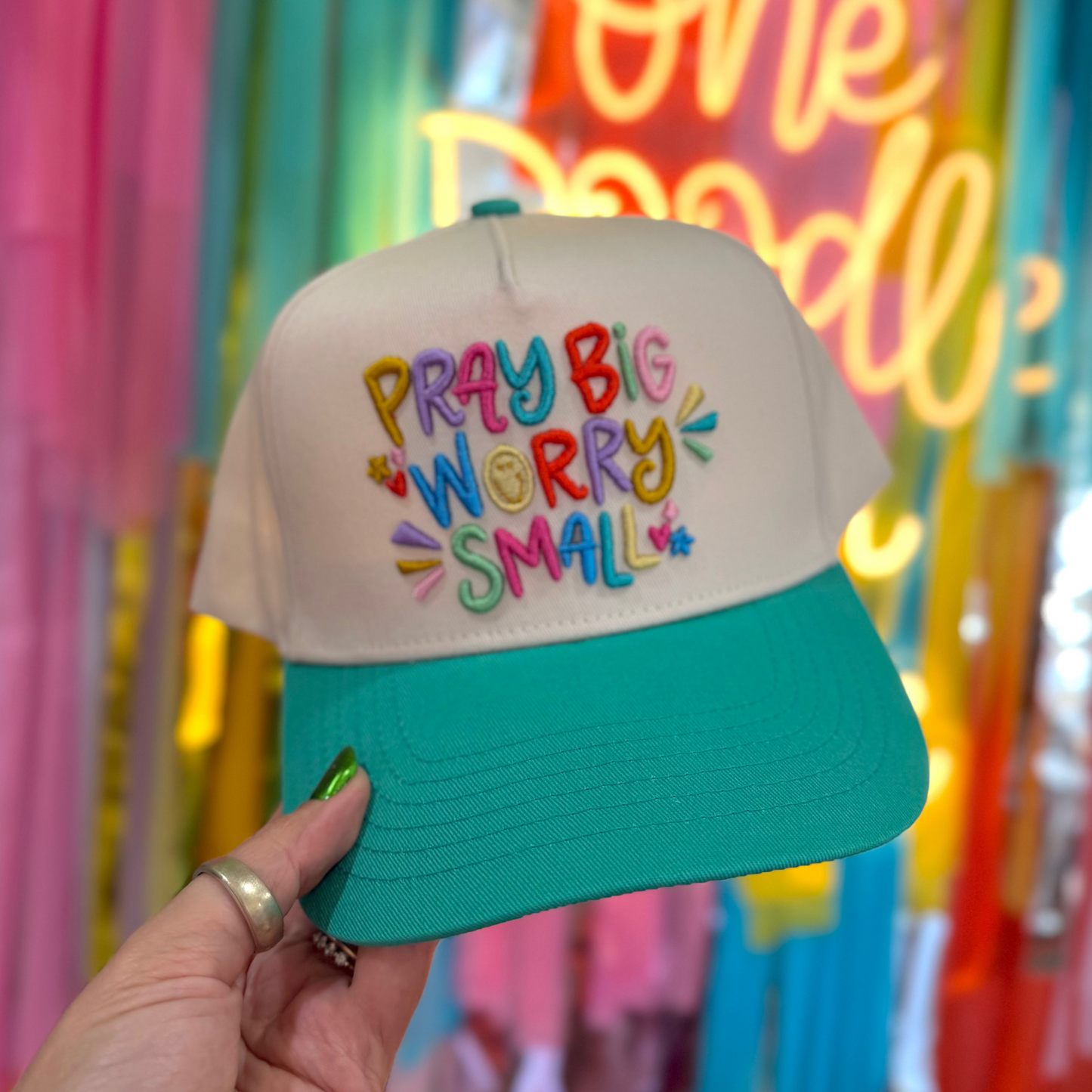 Cap with colorful text held in front of a vibrant, neon-lit background with balloons.