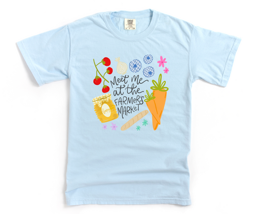 Light blue t-shirt with colorful graphics and 'meet me at the farmer's market' text on a white background