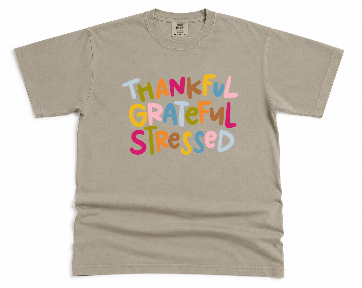Beige t-shirt with colorful text 'THANKFUL GRATEFUL STRESSED' on a white background