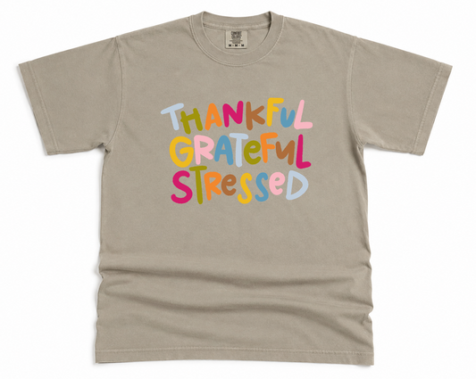 Beige t-shirt with colorful text 'THANKFUL GRATEFUL STRESSED' on a white background