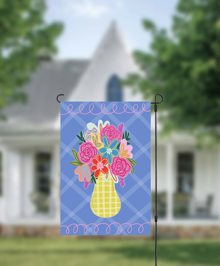 Decorative garden flag with colorful floral design on a blue background, displayed outdoors.