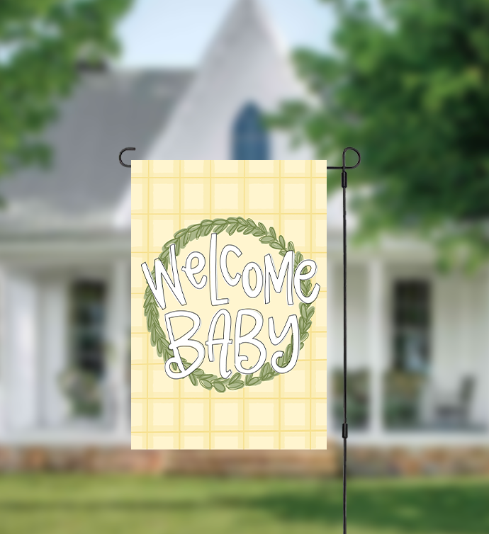 Decorative garden flag with 'Welcome Baby' text in front of a house