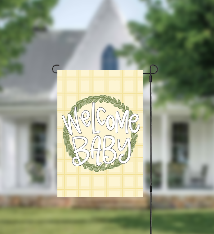 Decorative garden flag with 'Welcome Baby' text in front of a house