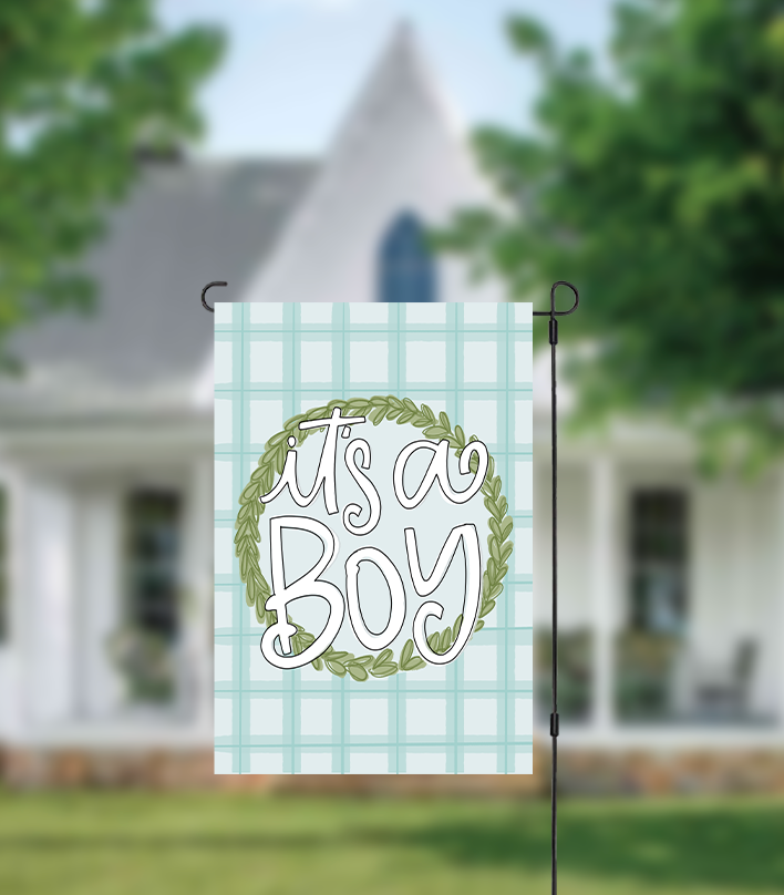 Decorative garden flag with 'It's a Boy' text on a plaid background in front of a house.