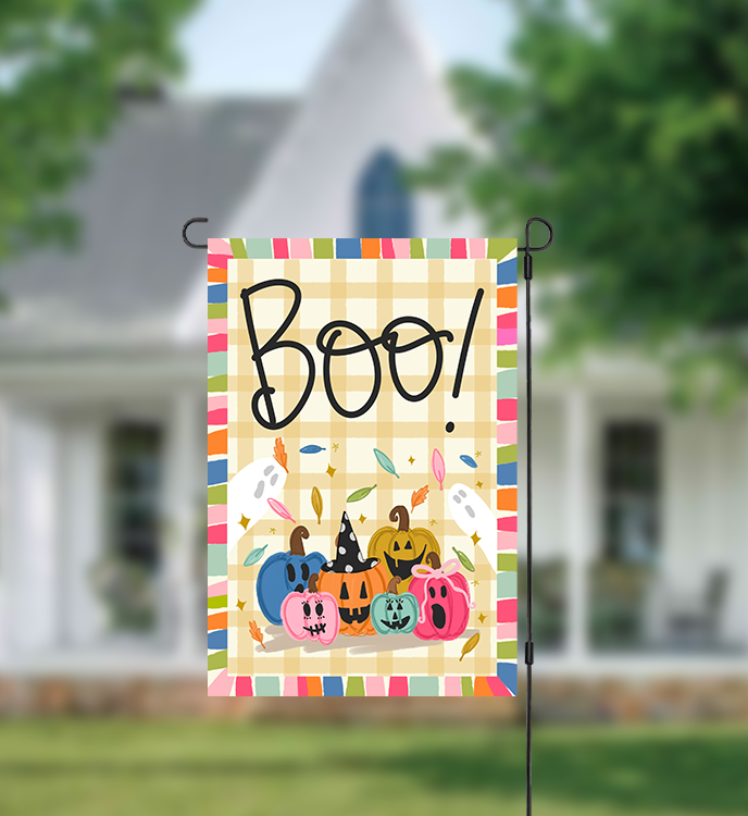 Decorative garden flag with 'Boo!' and pumpkins in front of a house.