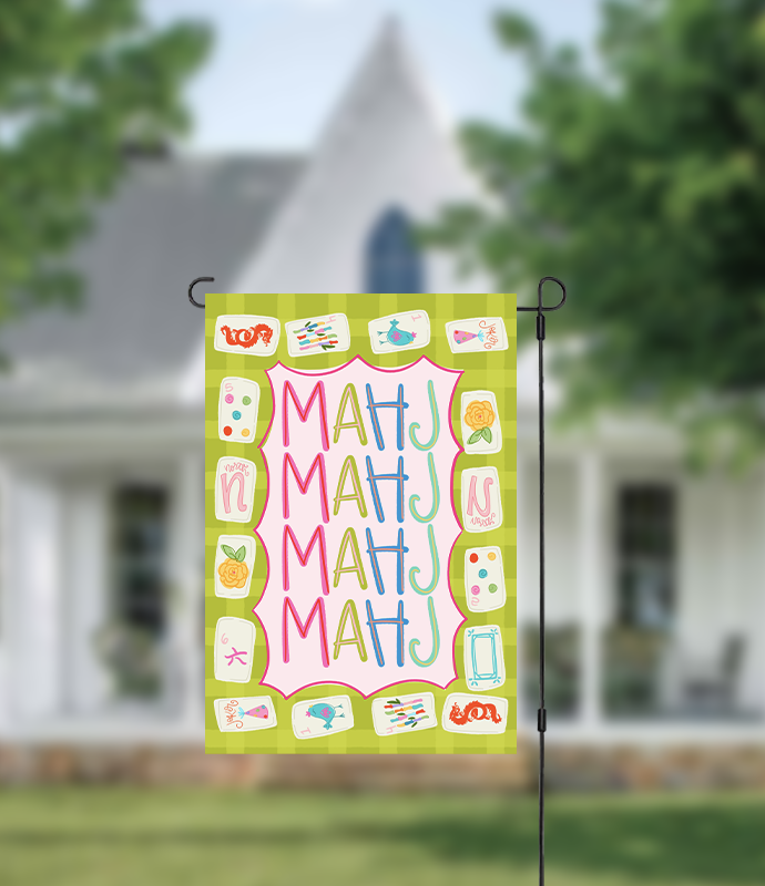 Decorative garden flag with colorful text and symbols on a green background, displayed outdoors.
