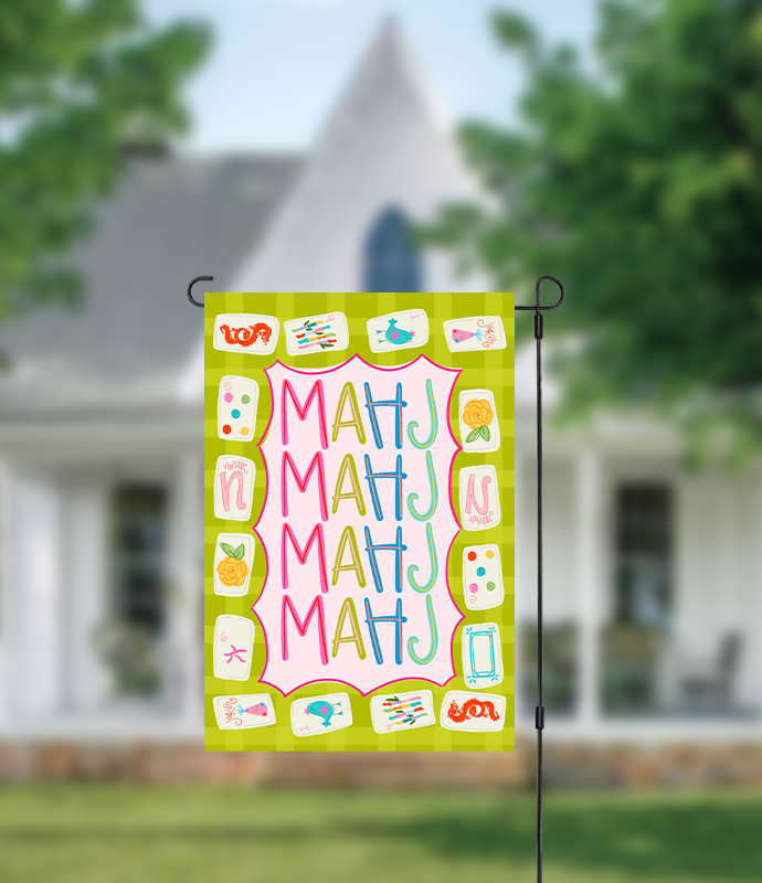 Decorative garden flag with colorful text and symbols on a green background, displayed outdoors.