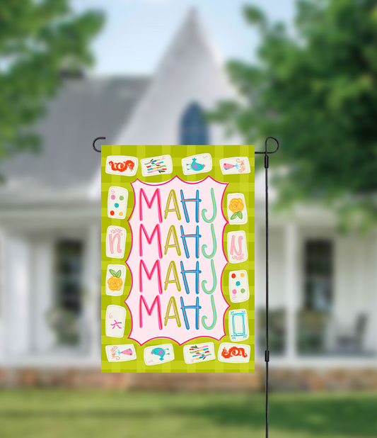 Decorative garden flag with colorful text and symbols on a green background, displayed outdoors.