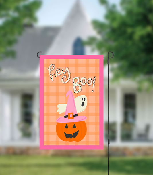 Halloween-themed garden flag with a pumpkin, ghost, and witch hat on a checkered background in front of a house.