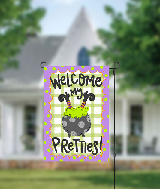 Decorative garden flag with 'Welcome my pretties!' text in front of a house.