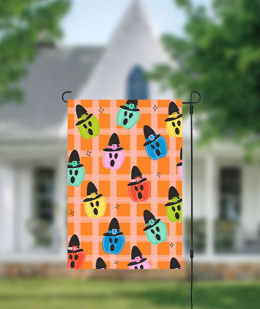 Halloween-themed garden flag with colorful ghosts on an orange checkered background, displayed outdoors.