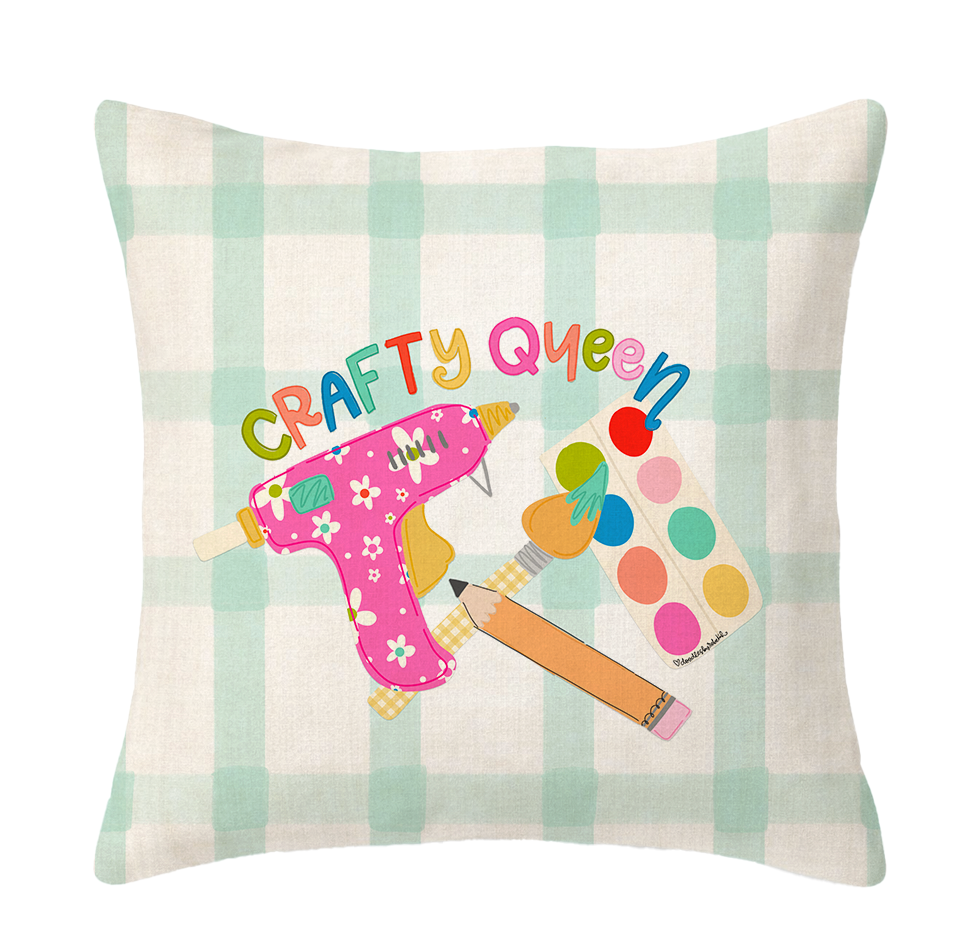 Decorative pillow with 'Crafty Queen' text and craft supplies on a plaid background