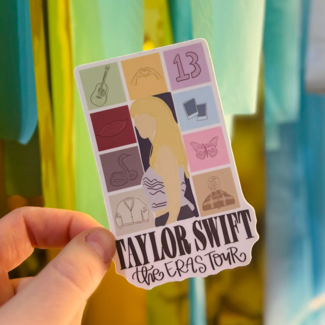 Doodles by Rebekah Taylor Swift The Eras Tour sticker. This hand-painted fan art vinyl decal features iconic symbols from Taylor Swift’s discography, making it the perfect gift for Swifties to decorate their water bottles, laptops, and journals.