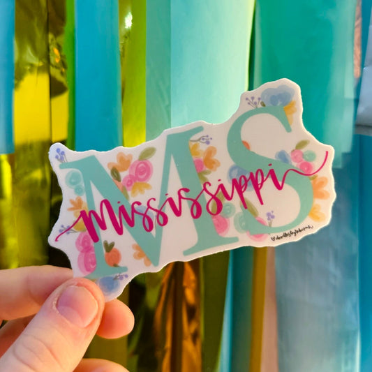 Doodles by Rebekah Mississippi "MS" state pride floral sticker. This whimsical hand-painted vinyl decal featuring botanical accents and pink script is a perfect gift for Mississippians to decorate water bottles, laptops, and planners.