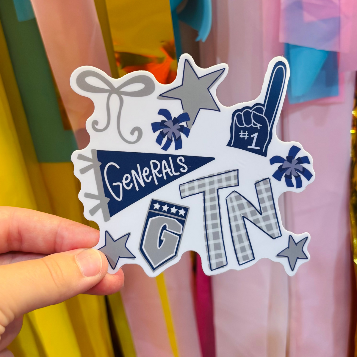 a hand holding a blue, grey, and white sticker with Tennessee Generals Game Day Iconography 