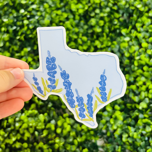 a hand holding a sticker of the outline of the state of text filled with bluebonnets