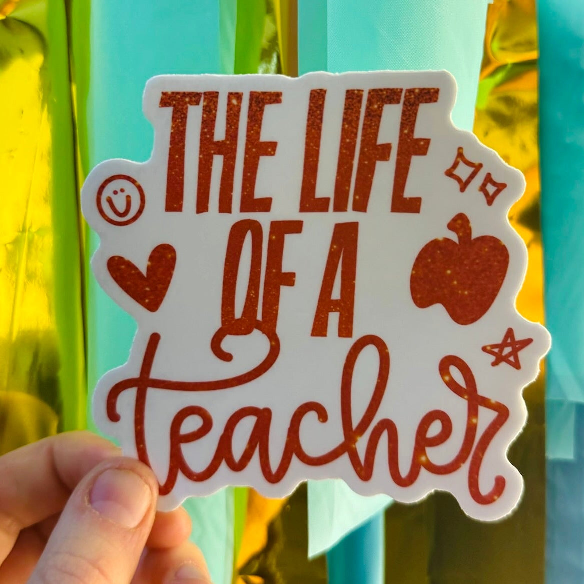 Doodles by Rebekah "The Life of a Teacher" sticker. This whimsical hand-painted vinyl decal features educational icons like an apple and stars, making it a perfect appreciation gift for teachers to decorate water bottles, laptops, and planners.