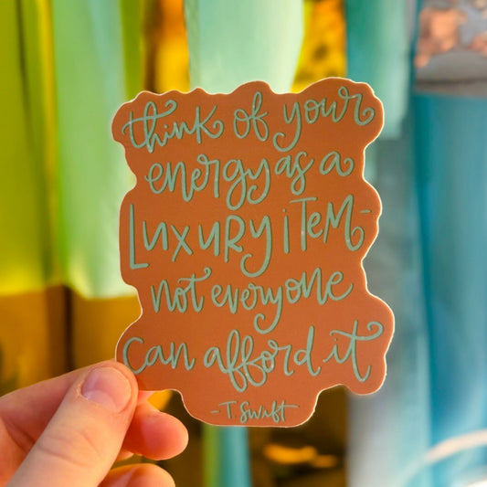Doodles by Rebekah Taylor Swift quote sticker. This hand-painted terracotta vinyl decal features the inspiring "energy as a luxury item" quote, making it a perfect motivational gift for Swifties to decorate water bottles, laptops, and journals.