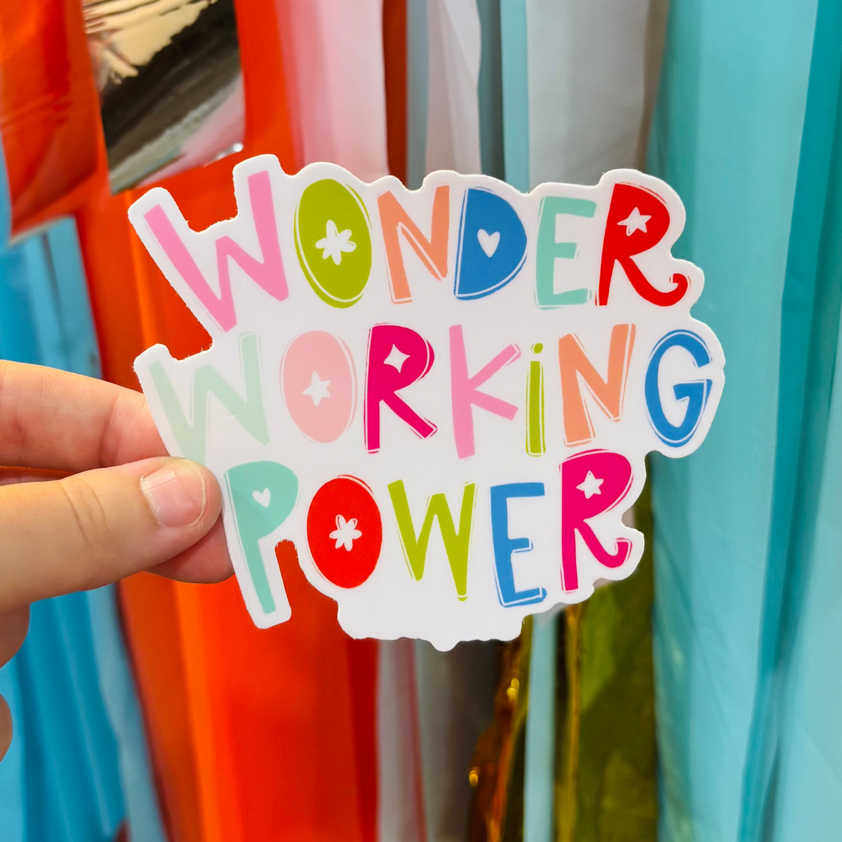 A hand holding a sticker that says "Wonder Working Power" in a bright, hand written font