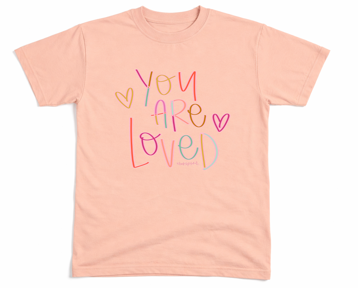 Pink t-shirt with 'You Are Loved' text on a white background