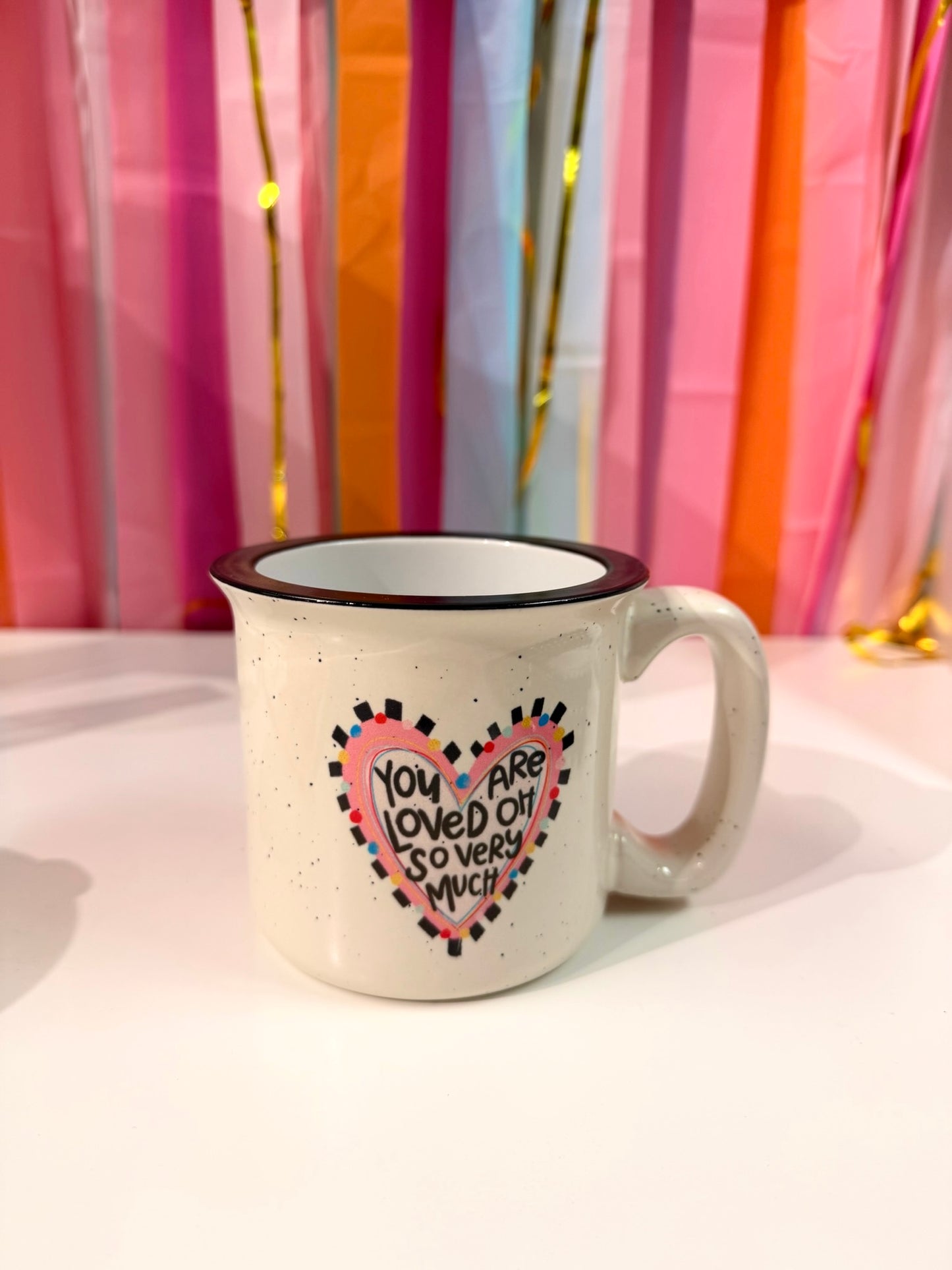 Doodles by Rebekah "You Are Loved" inspirational heart campfire mug. This whimsical hand-painted ceramic coffee cup features a colorful checkered heart design and serves as a perfect sentimental gift for Valentine's Day, anniversaries, or a sweet daily reminder for a loved one.
