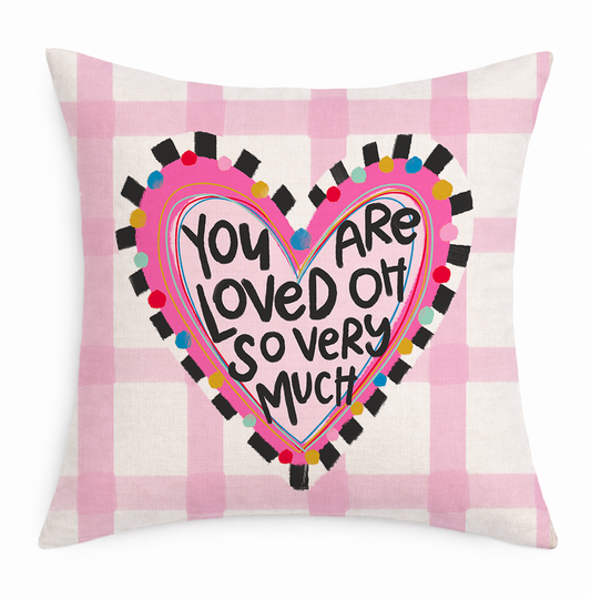 A pink and white gingham pillow with a decorative heart that says "You Are Loved Oh So Very Much Pillow" on a white background
