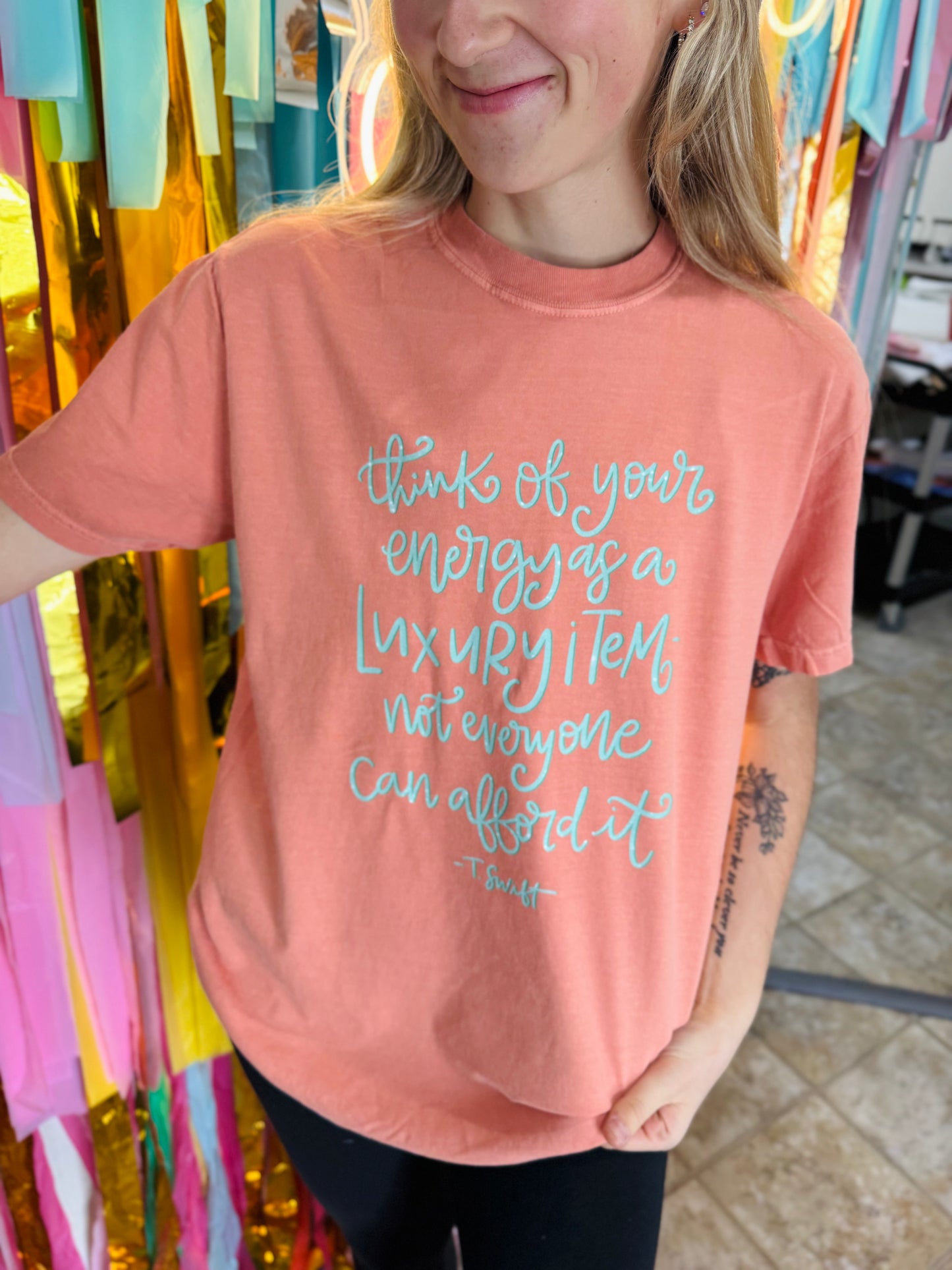 Person wearing a pink t-shirt with a motivational quote in a colorful store setting