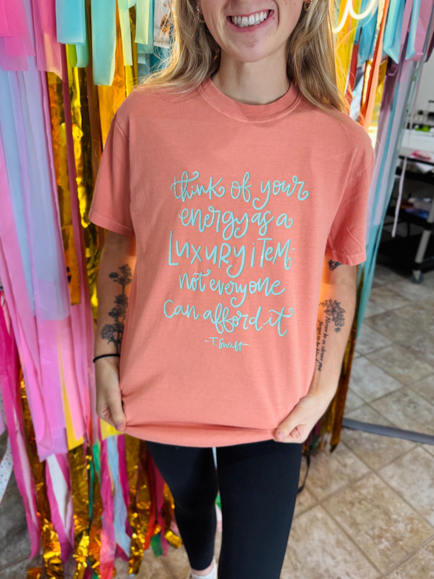 Person wearing a peach t-shirt with a quote in front of colorful streamers.