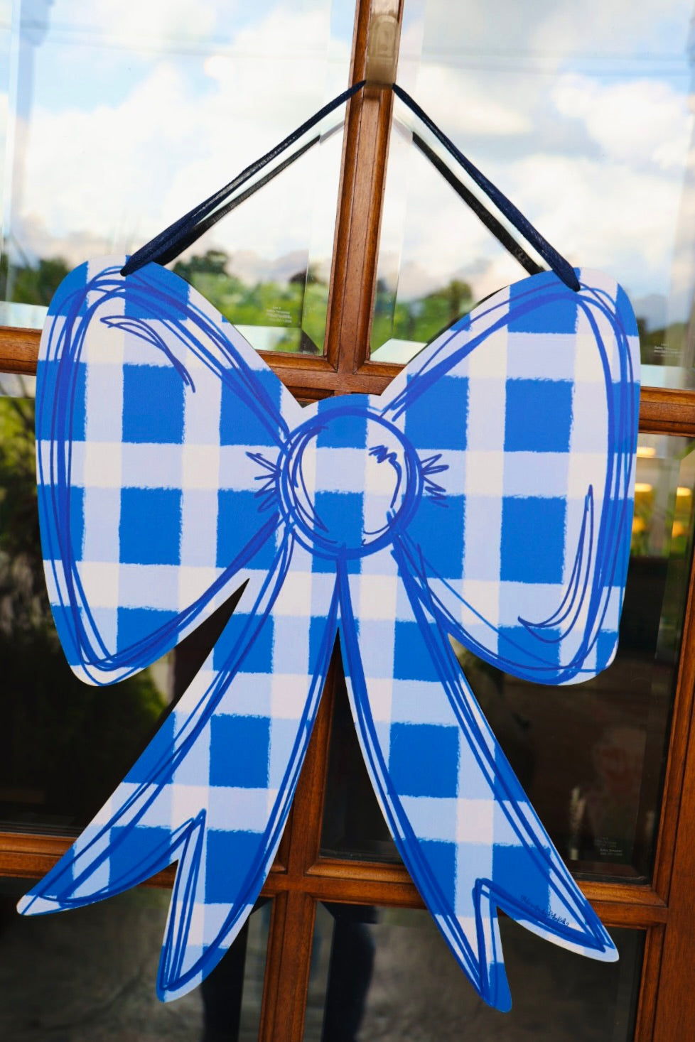 Blue and white checkered bow decoration hanging on a glass door.