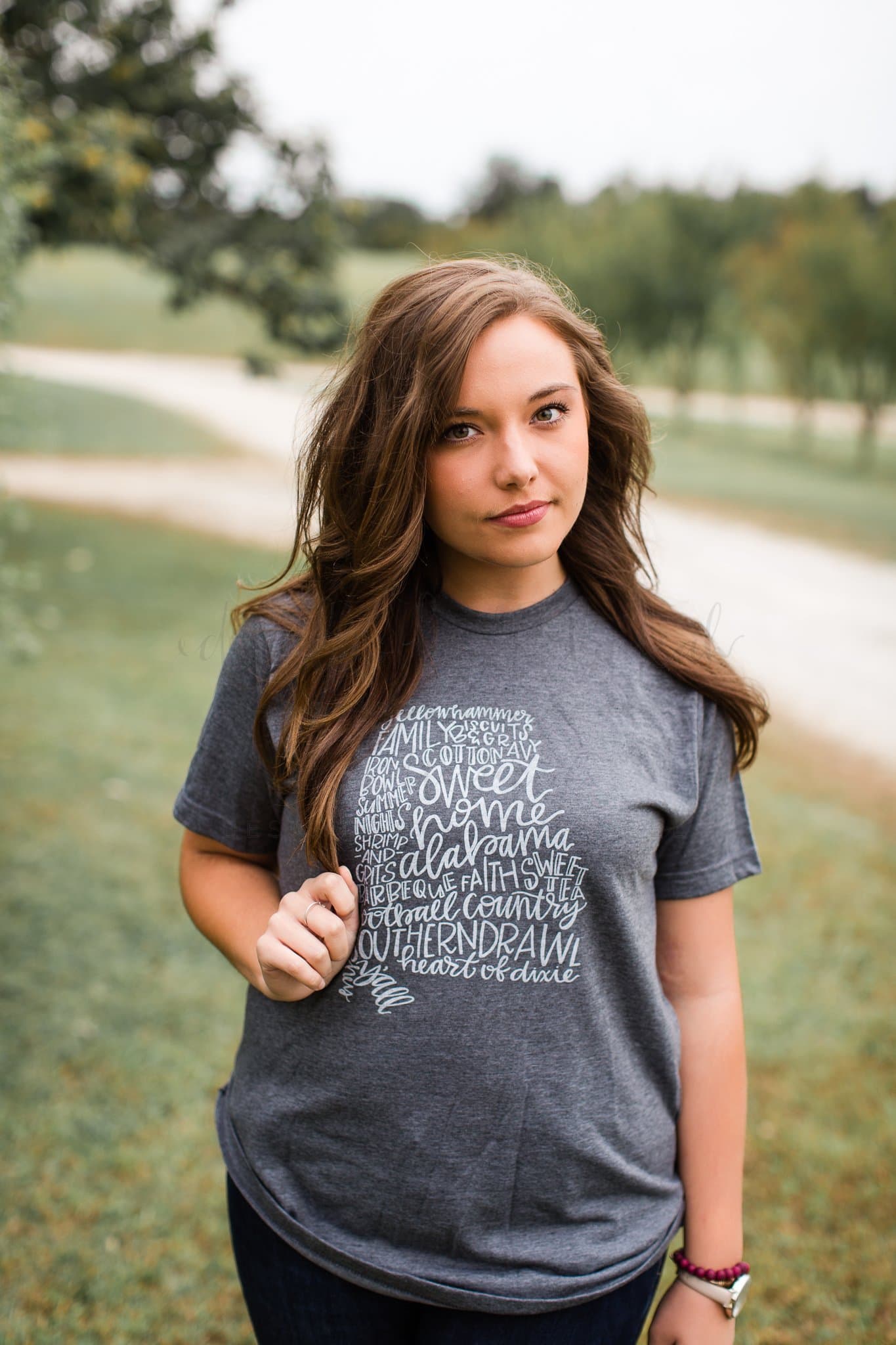 a woman standing outside in a charcoal T-shirt with the state of Alabama on it