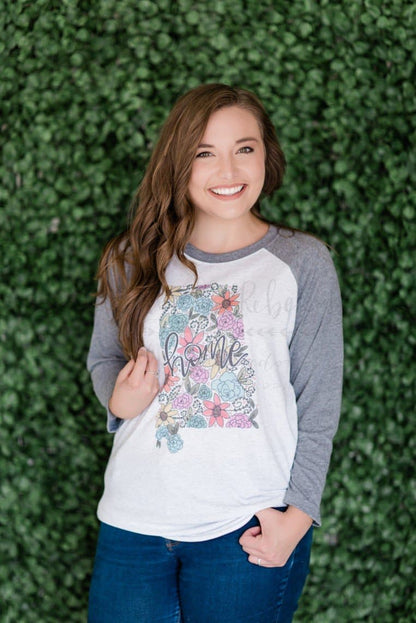 A person wearing a long-sleeved t-shirt with a floral design on the front, standing in front of a green leafy background.