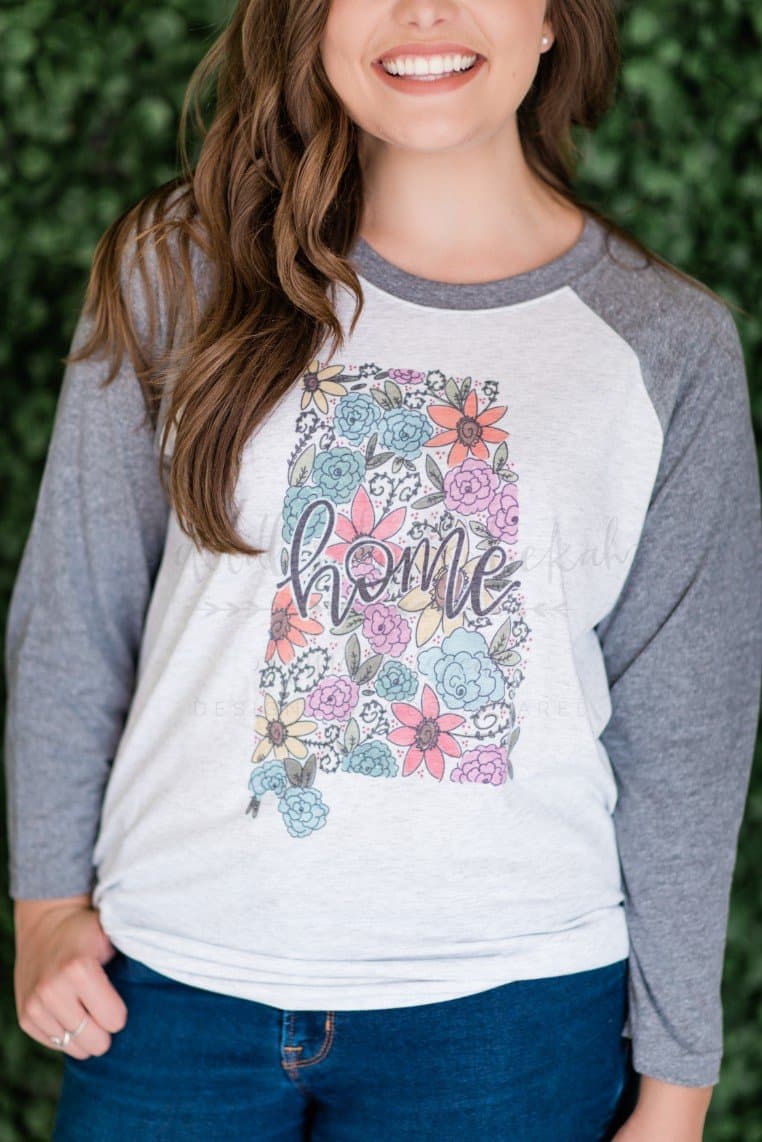 a woman standing with a raglan style shirt that reads Alabama over a floral outline of the state