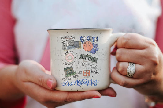 A person holding a white ceramic mug with multicolor speckles and various texts related to Lexington, KY.