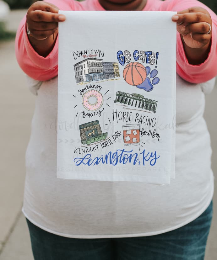 A white polyester tea towel with a colorful graphic print featuring text and illustrations related to Lexington, KY, and its attractions such as a doughnut, basketball, and a horse.