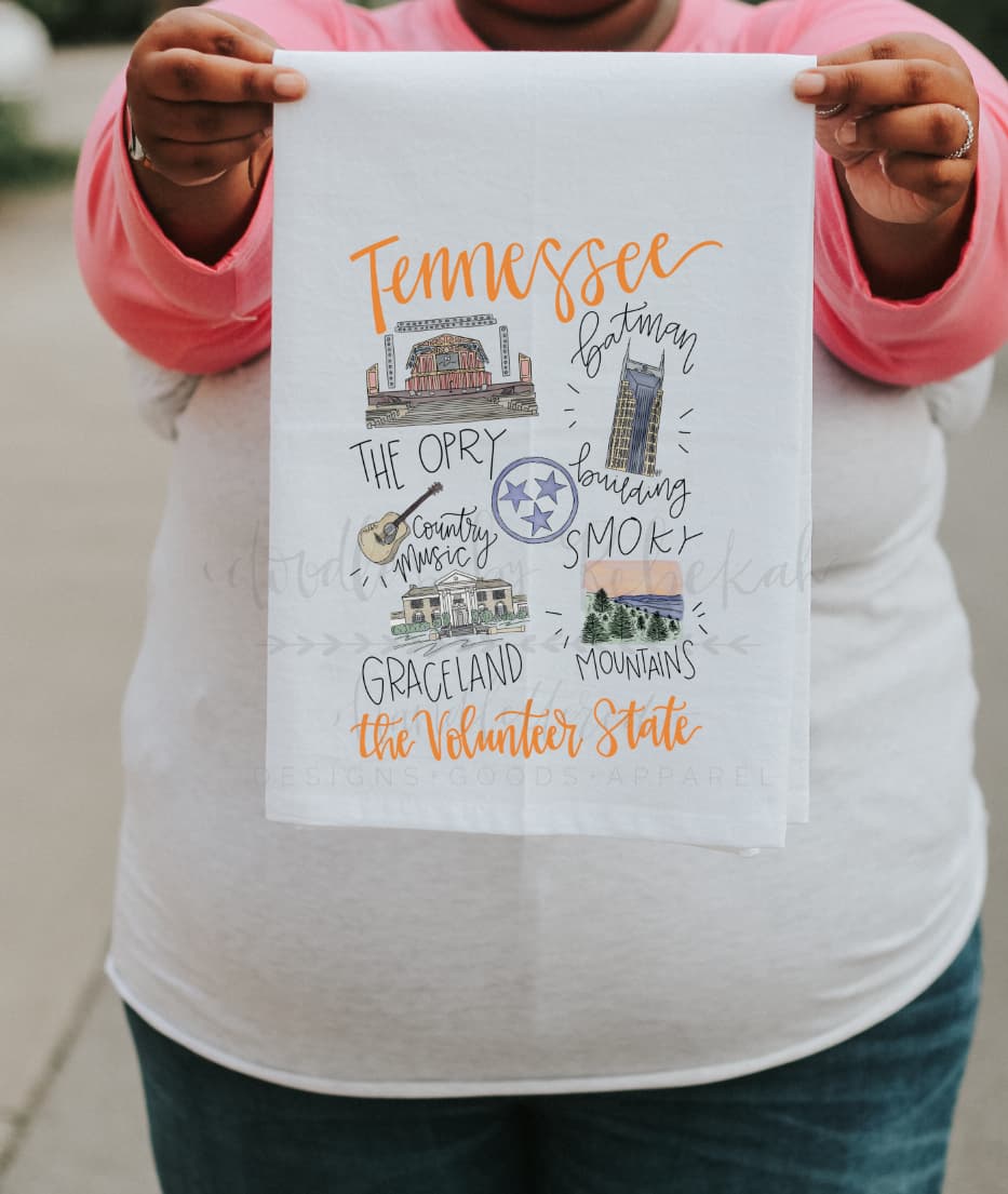 A person holding a white polyester tea towel with a map and text related to Tennessee, including the name 'The Volunteer State'.