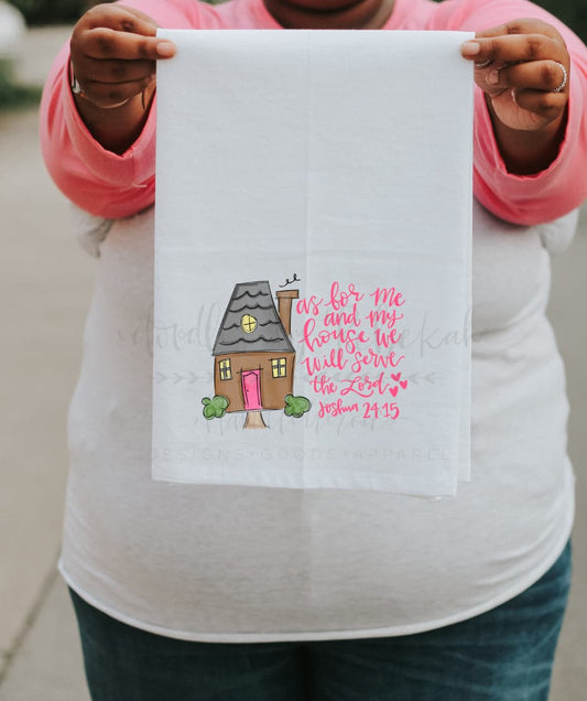 A person holding a white polyester tea towel with a printed religious message and a house illustration in pink.
