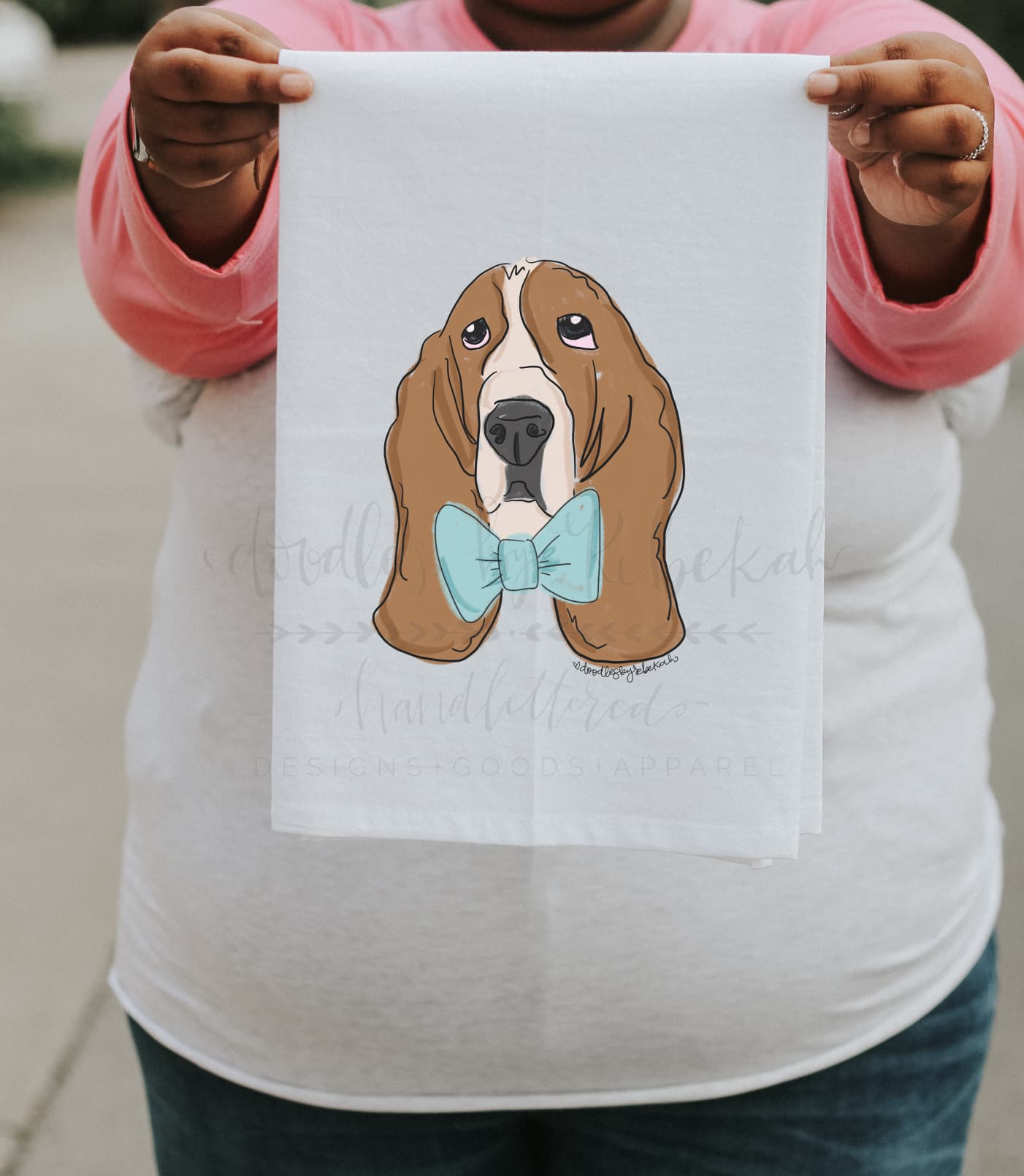 A person holding a white polyester tea towel with a printed basset hound wearing a bow tie.