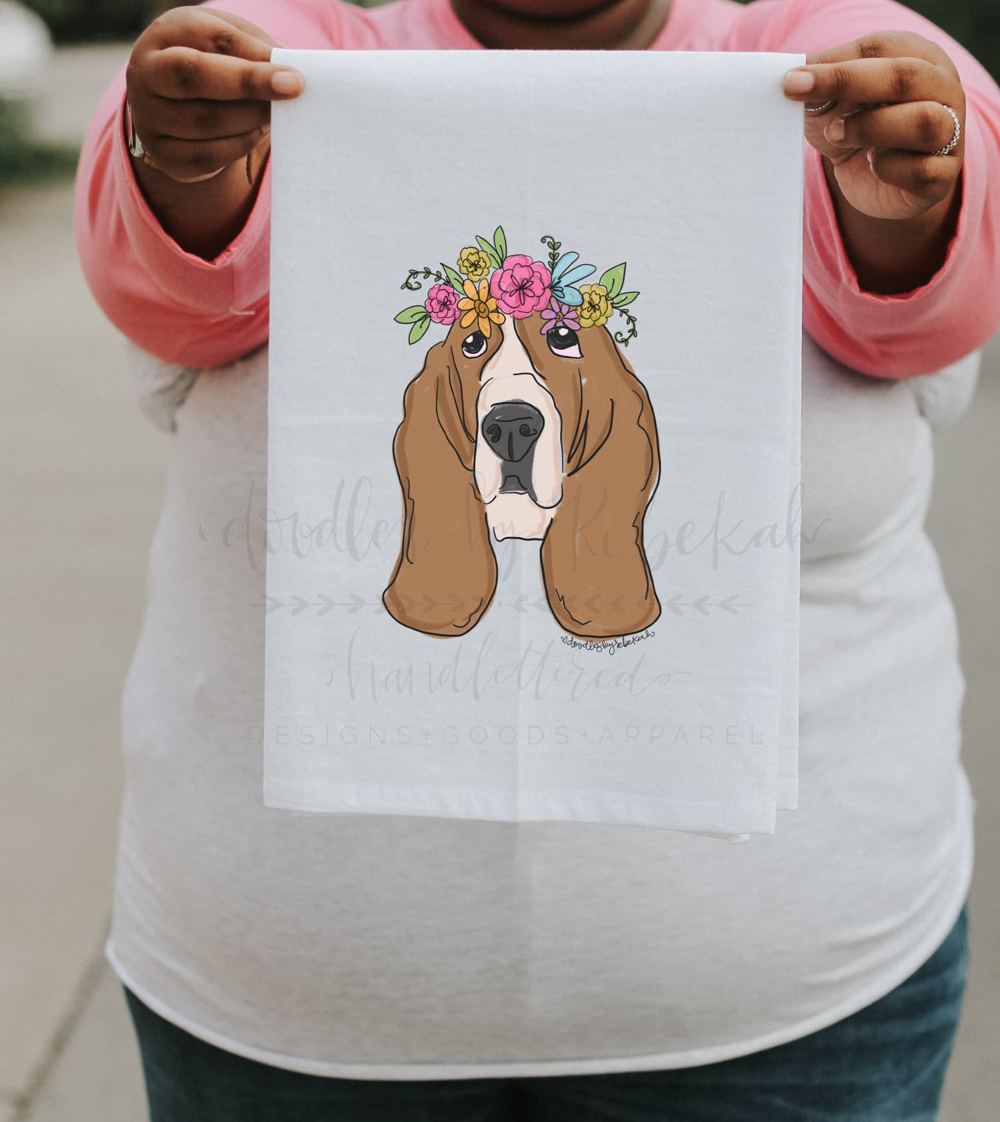 Close up of person holding a tea towel of a basset hound with a flower crown