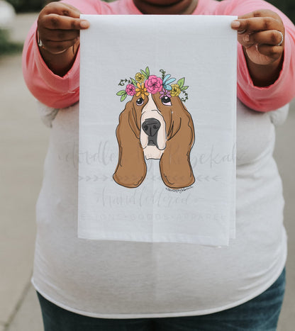 Close up of person holding a tea towel of a basset hound with a flower crown